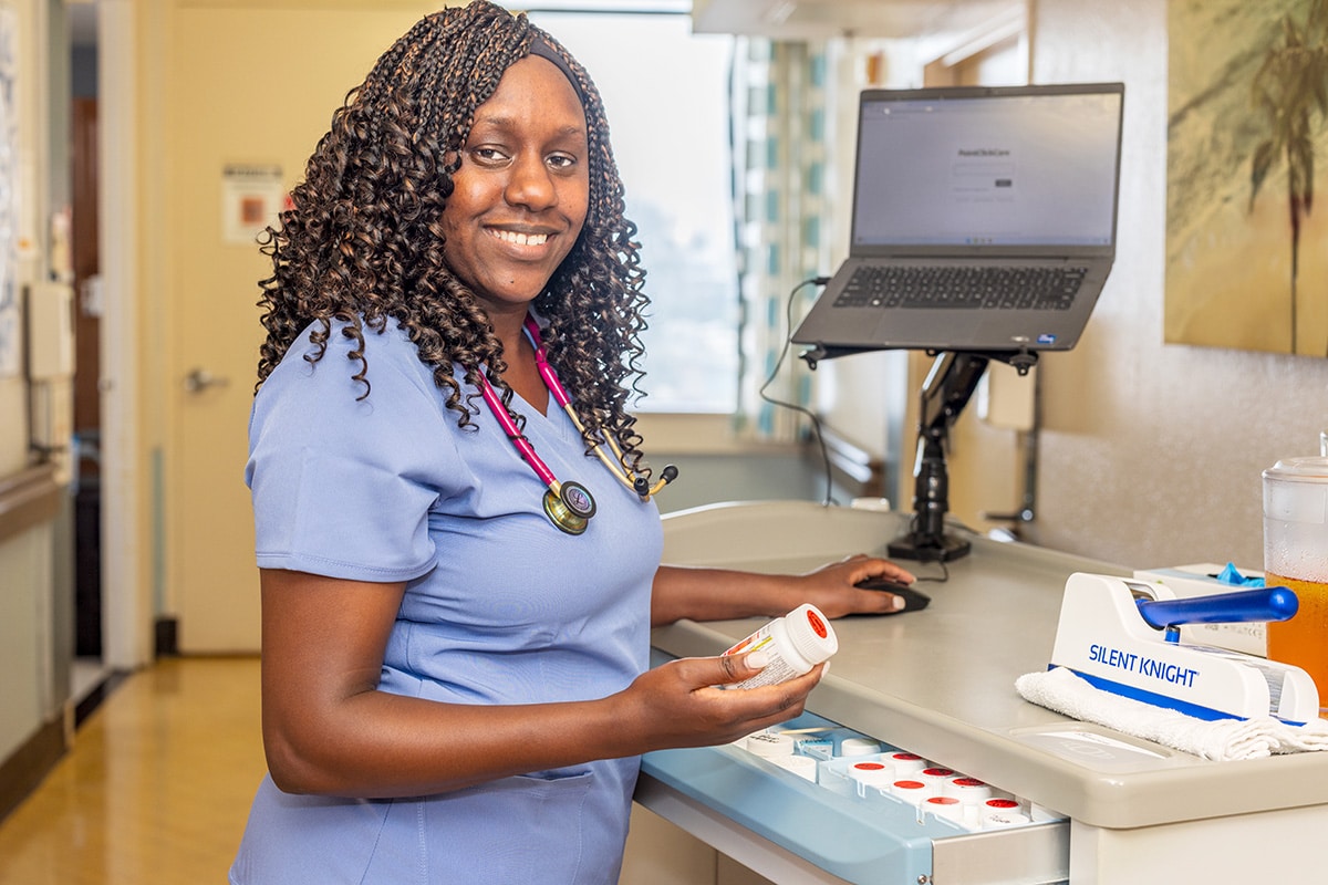 A caregiver standing in the hallway next to a nurse's cart at Beachwood Post-Acute and Rehab